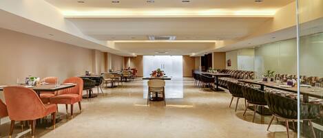 A spacious conference room with multiple tables and chairs, a central table with a floral arrangement, and a glass partition on one side.