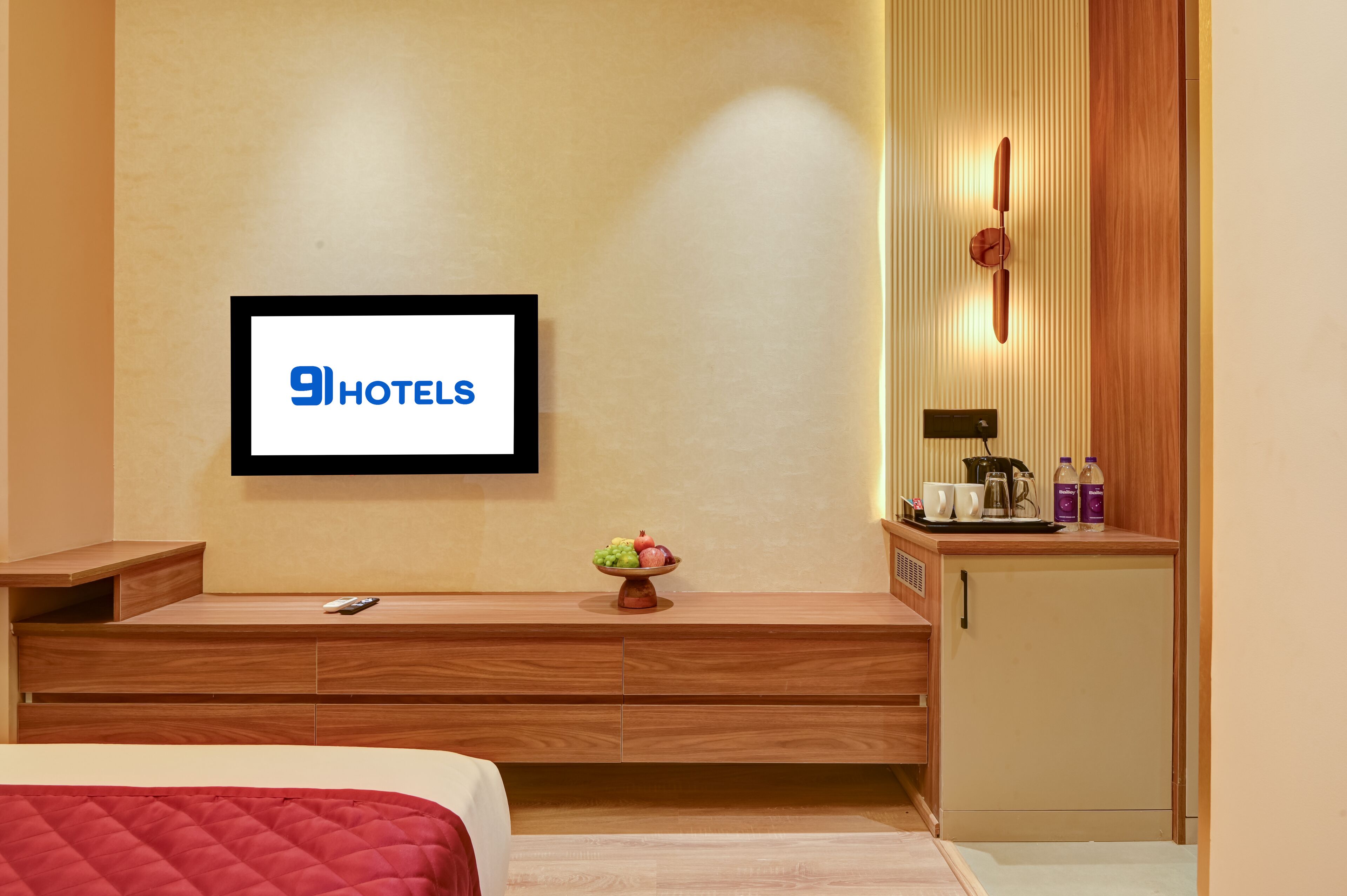 Una habitación de hotel moderna con cama, televisor montado en la pared, una mesita consola de madera, un armario pequeño y un frutero.