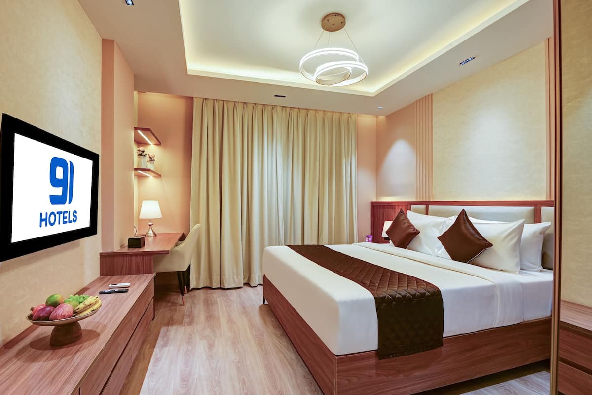 Hotelkamer met een bed, bureau met lamp, een televisiescherm waarop '9 HOTELS' staat en een fruitmand op het bureau.
