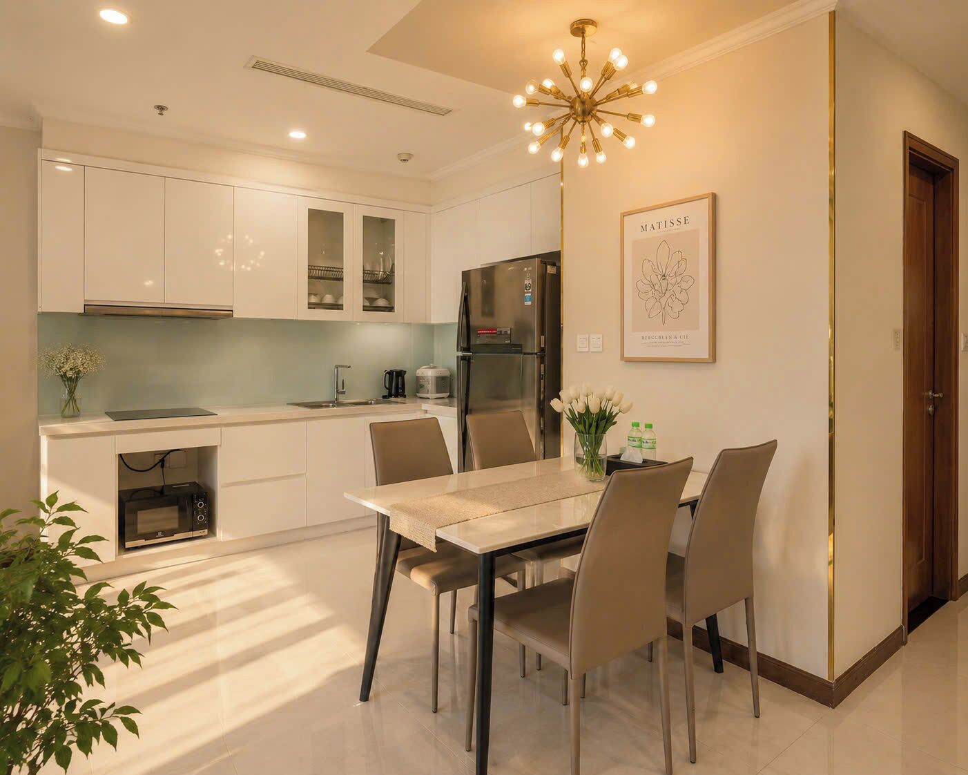 A modern kitchen with white cabinets, a stainless steel refrigerator, and a dining area with a table and chairs.
