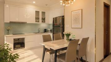 A modern kitchen with white cabinets, a stainless steel refrigerator, and a dining area with a table and chairs.