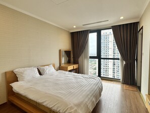 A hotel room with a large bed, a wooden nightstand, a mirror, and a view of a cityscape through a large window with curtains. - Vinhomes Royal City by Emily in Town (Hanoi)