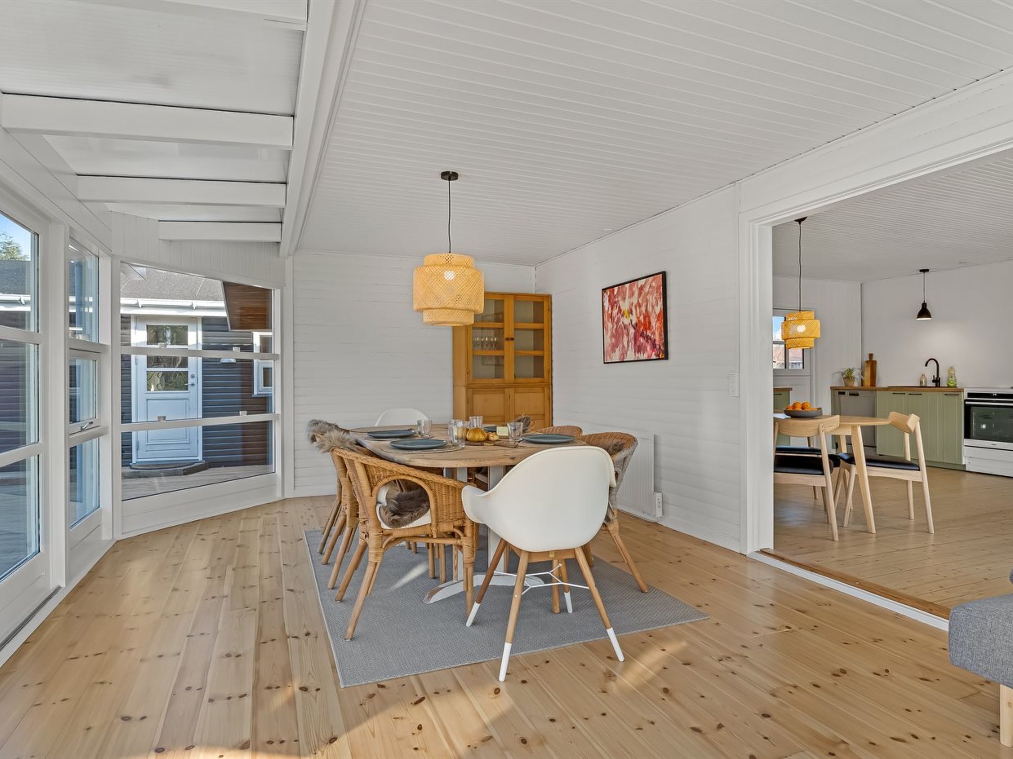 A modern dining area with a wooden table, wicker chairs, and a yellow pendant light.