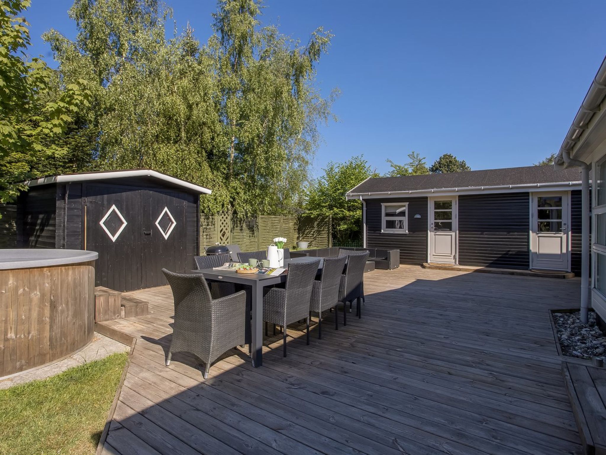 A deck with outdoor furniture and a barbecue area, surrounded by a wooden fence and trees.