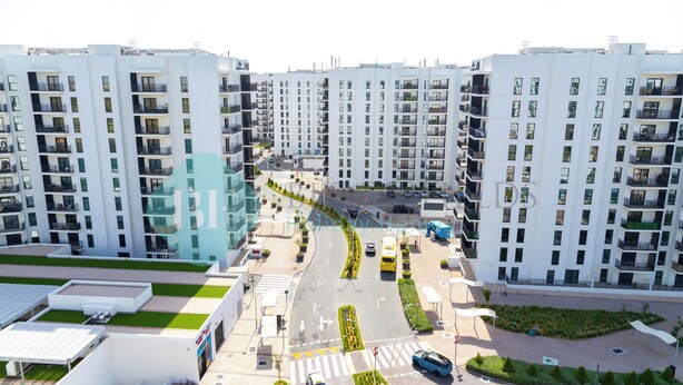 A modern apartment complex with multiple high-rise buildings, a central road with vehicles, and green landscaping. - Bloomfields STU Partial Canal View  (Abu Dhabi)
