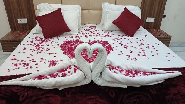 Ein Bett mit Rosenblättern und einer Handtuchherz-Dekoration, weißen Kissen und einem Holzkopfstück.