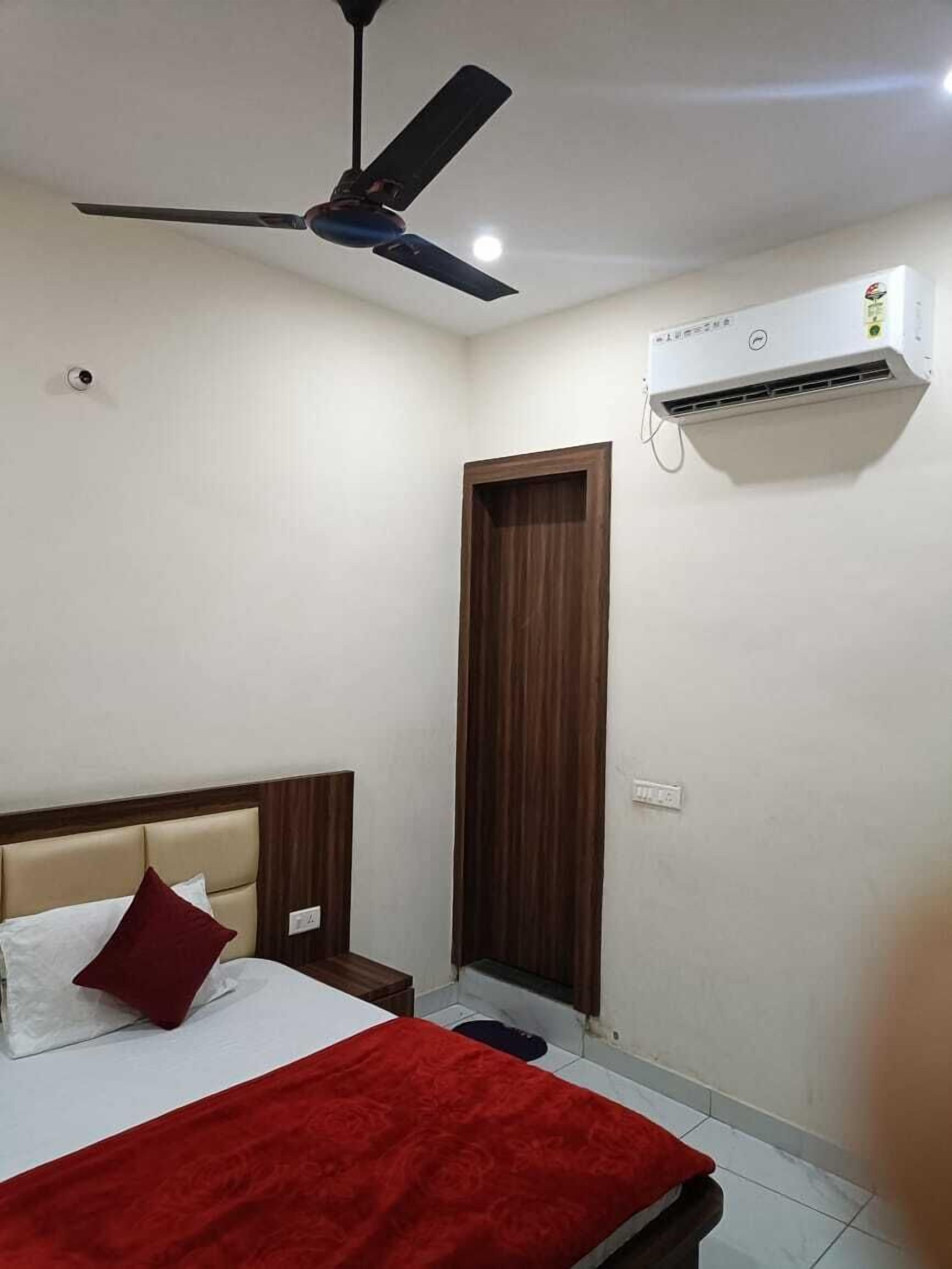 A bedroom with a bed, a ceiling fan, an air conditioning unit, and a door.