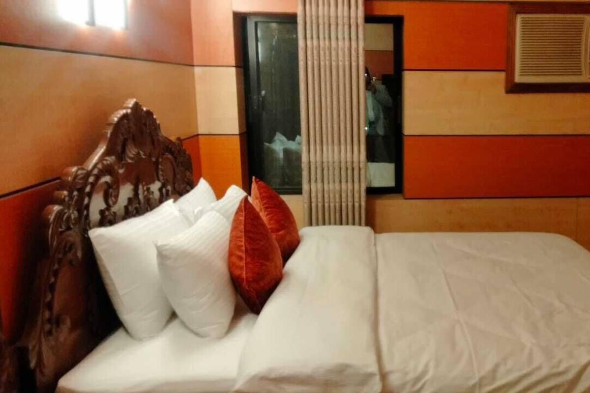 A hotel room with a large bed, a wooden headboard, and a window with curtains.