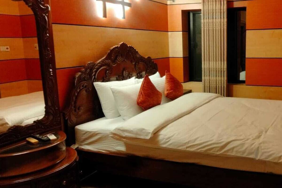 A hotel room with a large bed, a wooden headboard, and a bedside table with a lamp.