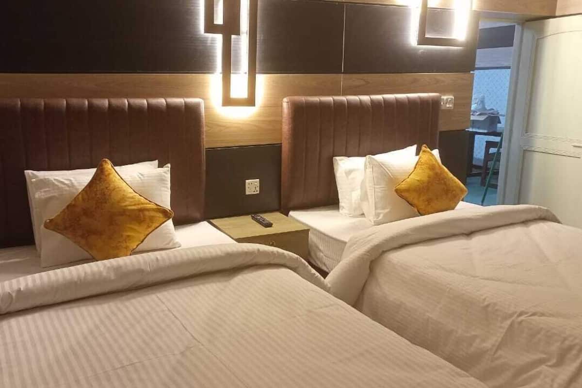 A hotel room with two beds, each with a headboard, white bedding, and a single pillow.