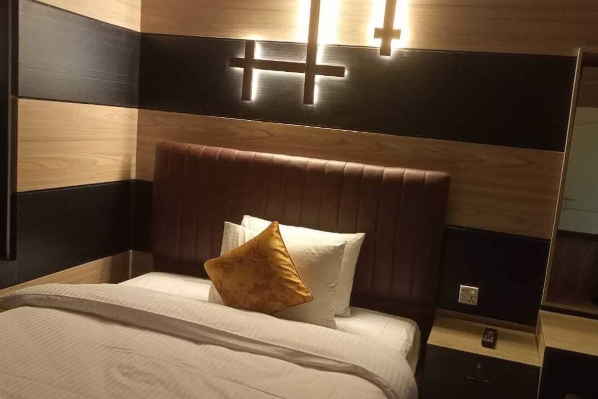 A hotel room with a bed, a nightstand, a mirror, and a cross-shaped light fixture on the wall.
