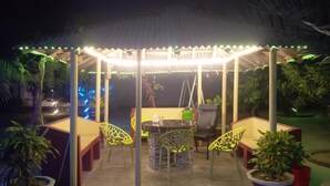 An outdoor patio area with a covered seating area, tables, chairs, and potted plants. - Garden View Villa (Rajshahi)