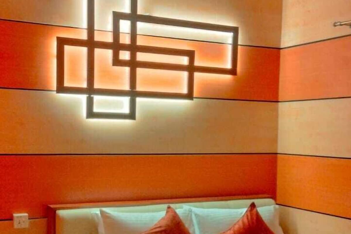 A modern bedroom with a large bed, orange walls, and a geometric light fixture.