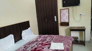 Habitación de hotel con cama, armario de madera, televisión montada en la pared y una mesita.