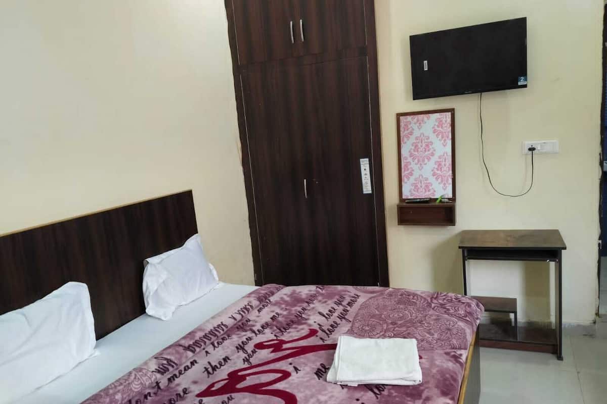 Habitación de hotel con cama, armario de madera, televisión montada en la pared y una mesita.