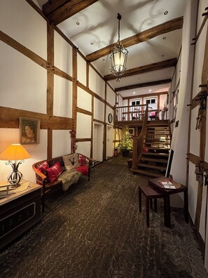 A traditional interior with exposed wooden beams, a staircase, a sofa with red cushions, and a hanging lamp.
