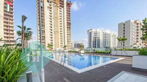 Una piscina en la azotea con cubierta de madera, rodeada de edificios altos y algo de vegetación.