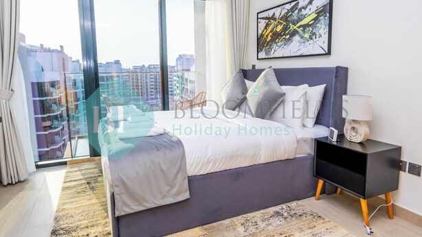 Un dormitorio moderno con una cama grande, una mesita de noche y vistas de la ciudad a través de un ventanal amplio.