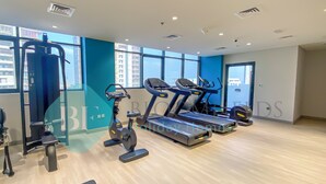 Un gimnasio moderno con máquinas de cardio, equipo de entrenamiento con pesas y grandes ventanales que ofrecen vistas de la ciudad.