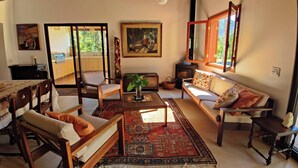 A spacious living room with a sofa, chairs, a coffee table, and a rug. There is a painting on the wall and a window with a view of greenery. - Paradisiacal Site in National Park (Teresópolis)