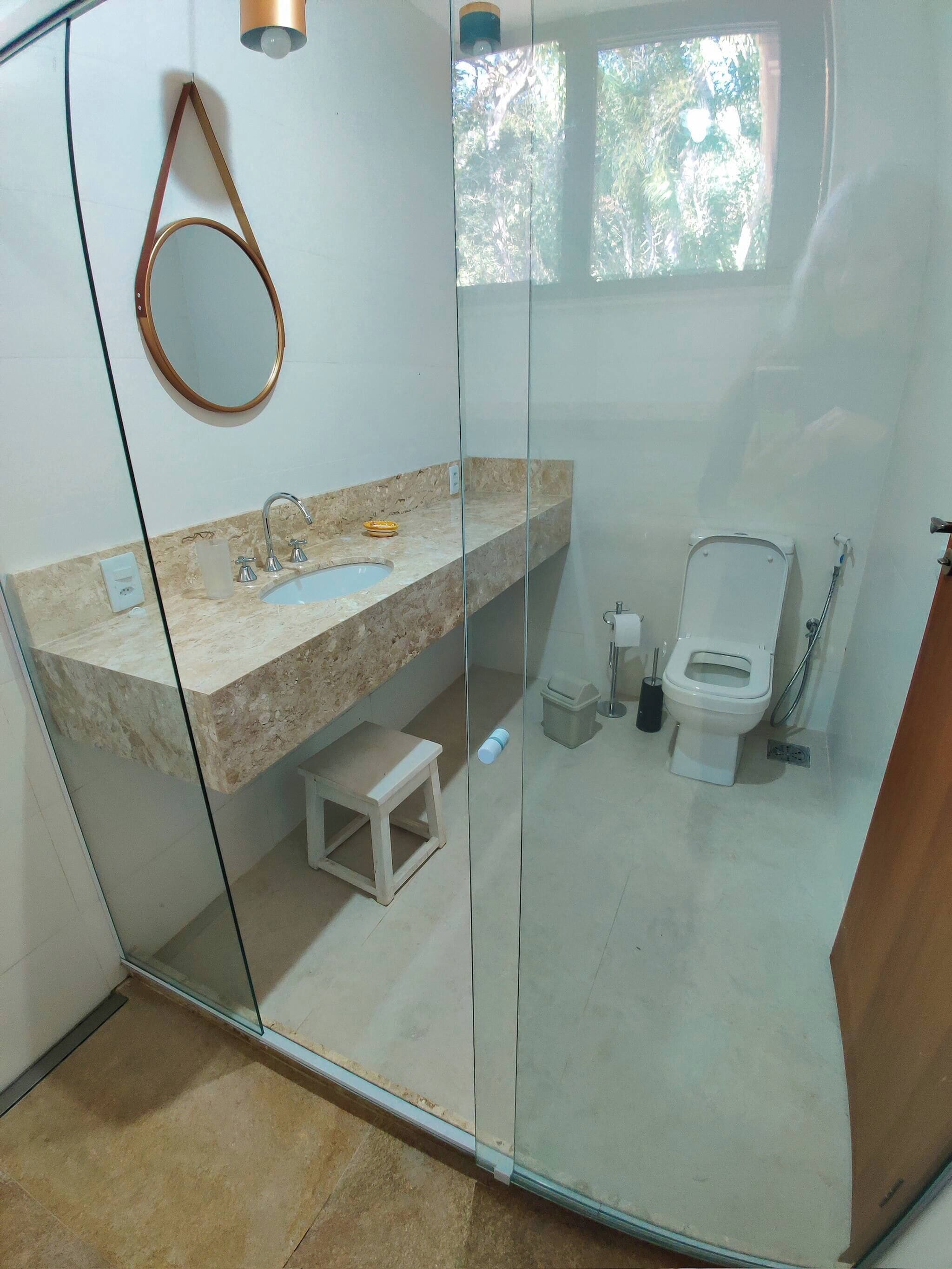 A modern bathroom with a glass partition, a marble sink, a toilet, and a small step stool.