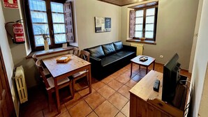 A cozy living room with a black leather sofa, wooden table, and a tiled floor.