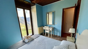 A bedroom with a bed, a desk, a chair, a mirror, and a view of mountains through large windows.