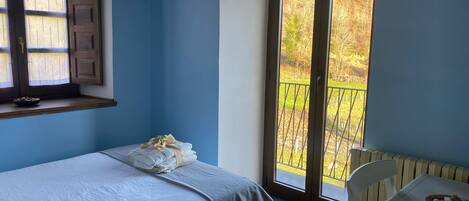 Ein Schlafzimmer mit Bett, einem Fenster mit Holzläden, einem Balkon mit Metallgeländer und einem weißen Stuhl.