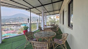 A covered outdoor area with a round table and wicker chairs, surrounded by artificial grass. - SIDDHI VINAYAK HOTEL AND BANQUET (Bhimtal)