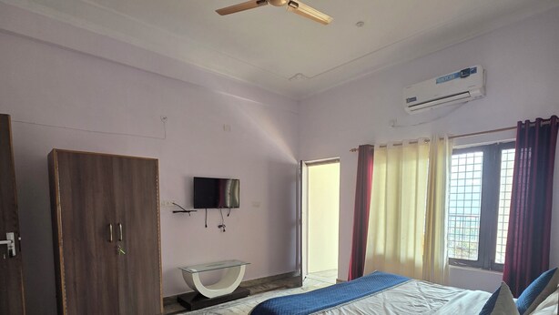A bedroom with a bed, a wardrobe, a television, and an air conditioning unit. - SIDDHI VINAYAK HOTEL AND BANQUET (Bhimtal)