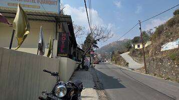 A motorcycle parked on the roadside, a sign for the HHI VINAYAK HOTEL & BANQUET, and a road leading into the distance.