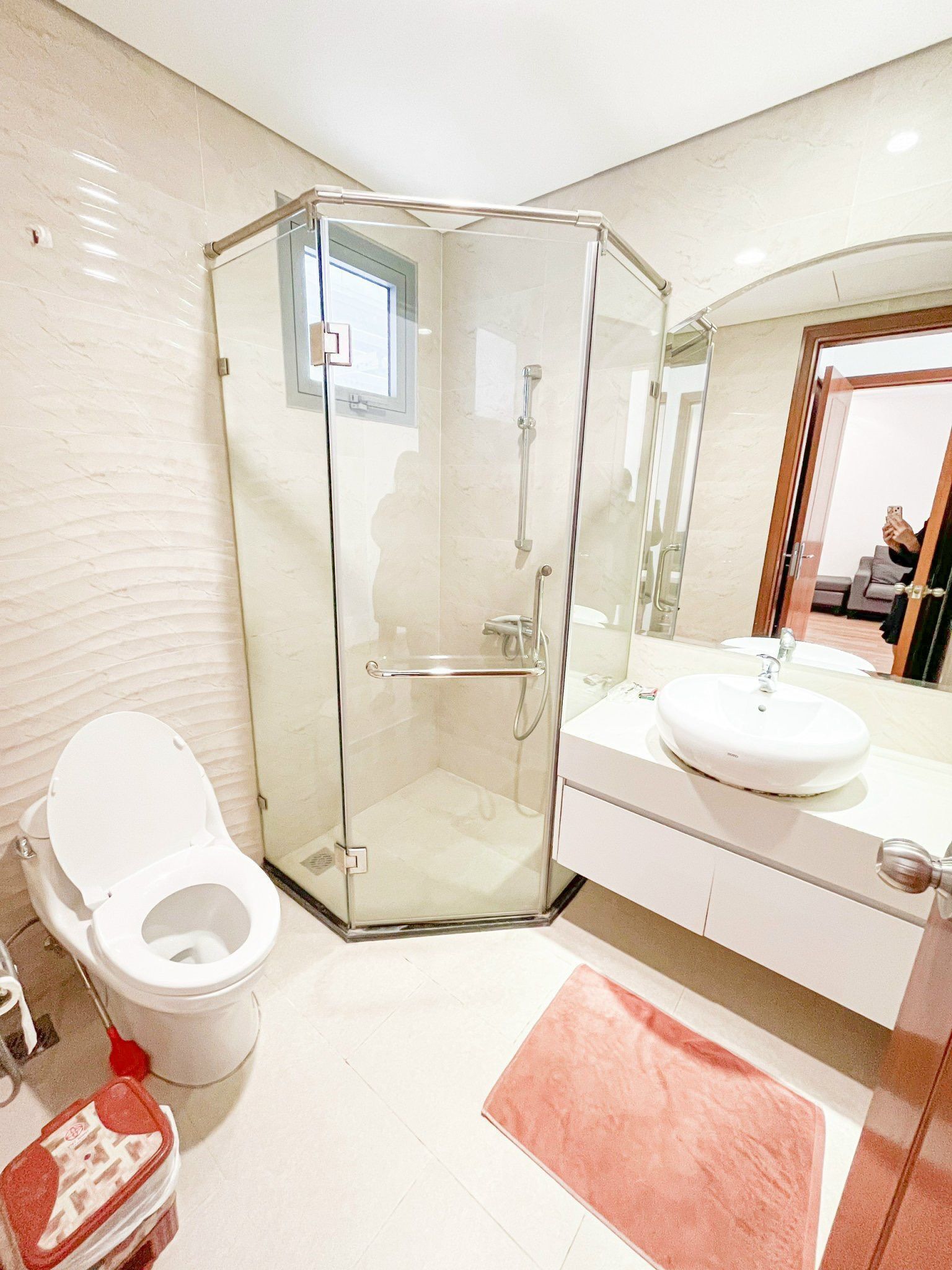Un baño moderno con ducha de vidrio, inodoro blanco y lavamanos con espejo.