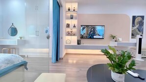 Een moderne slaapkamer met een bed, een televisie, een bureau en een plant.