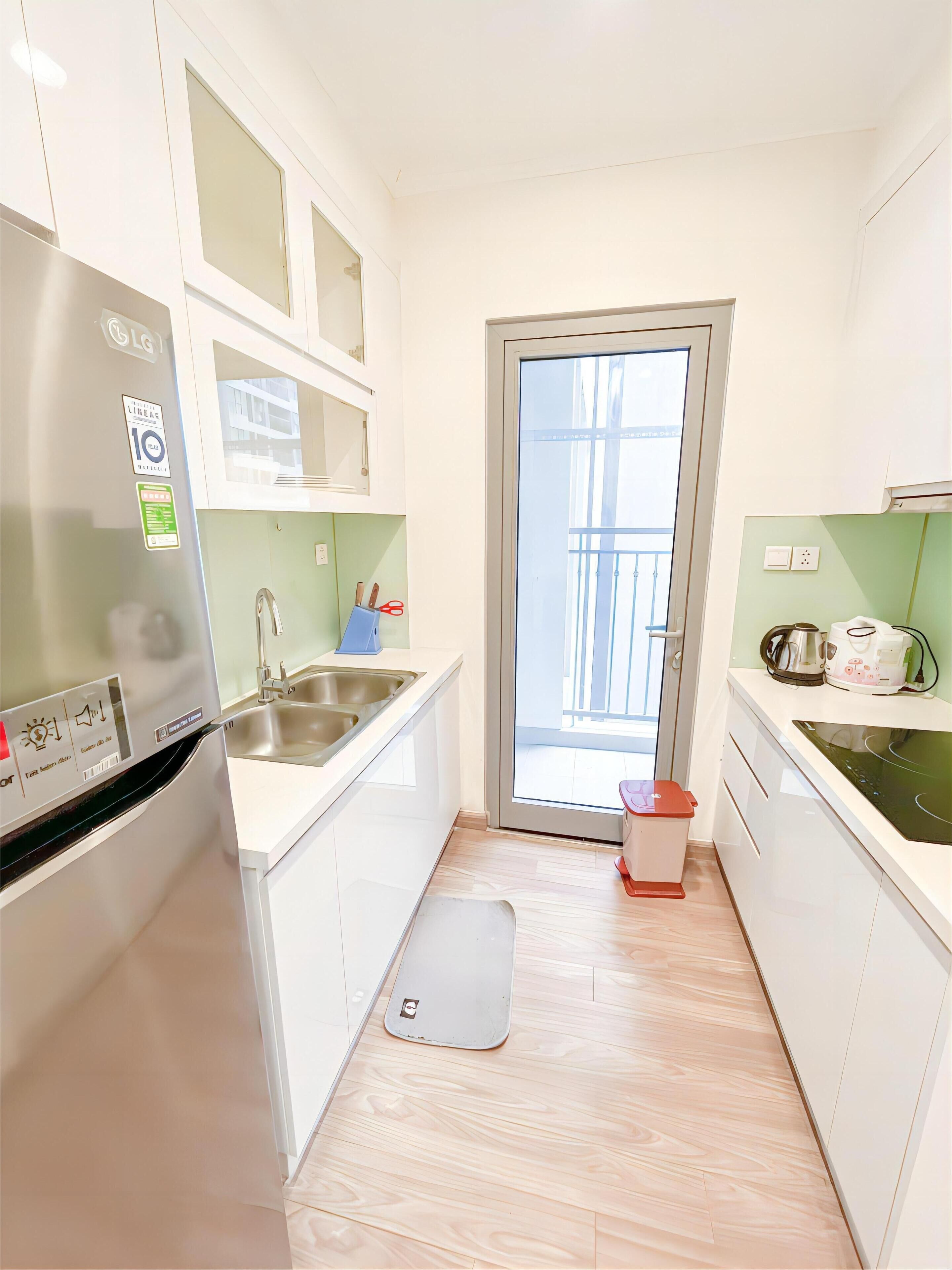 A compact kitchen with white cabinets, a stainless steel sink, a built-in oven, and a small countertop with a kettle and toaster.