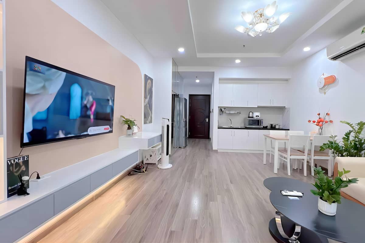 Un saló modern amb televisió de pantalla plana, un sofà, una taula de centre i una zona de cuina amb armaris blancs i una taula de menjador.