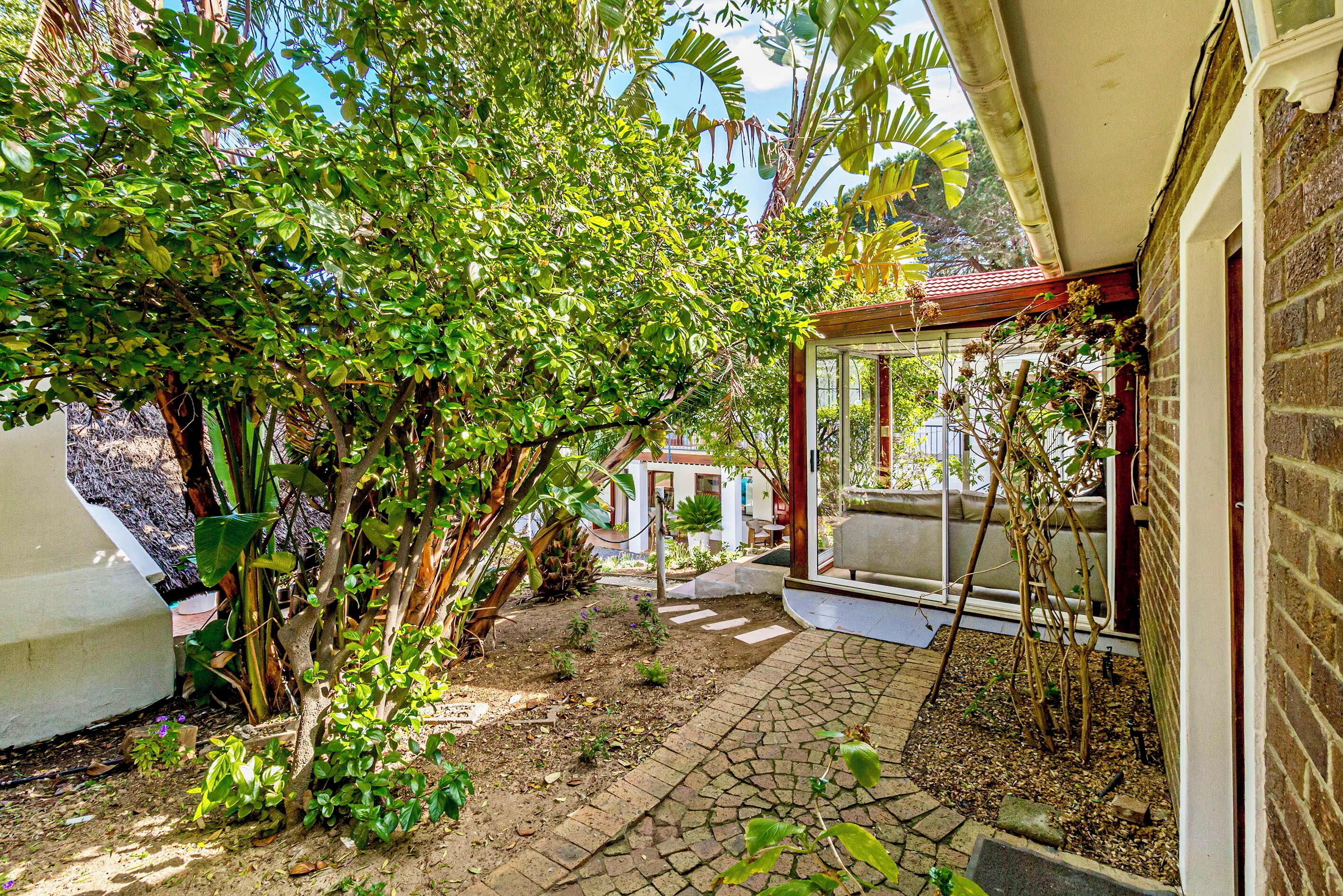 Un jardin avec un chemin en briques menant à une zone abritée dotée d’une porte en verre.