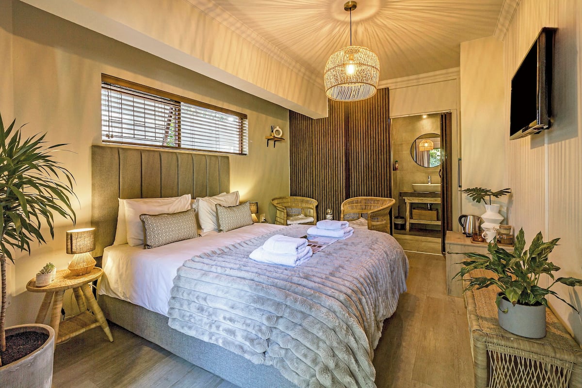 A modern bedroom with a large bed, bedside tables, a TV, and a bathroom visible through an open door.
