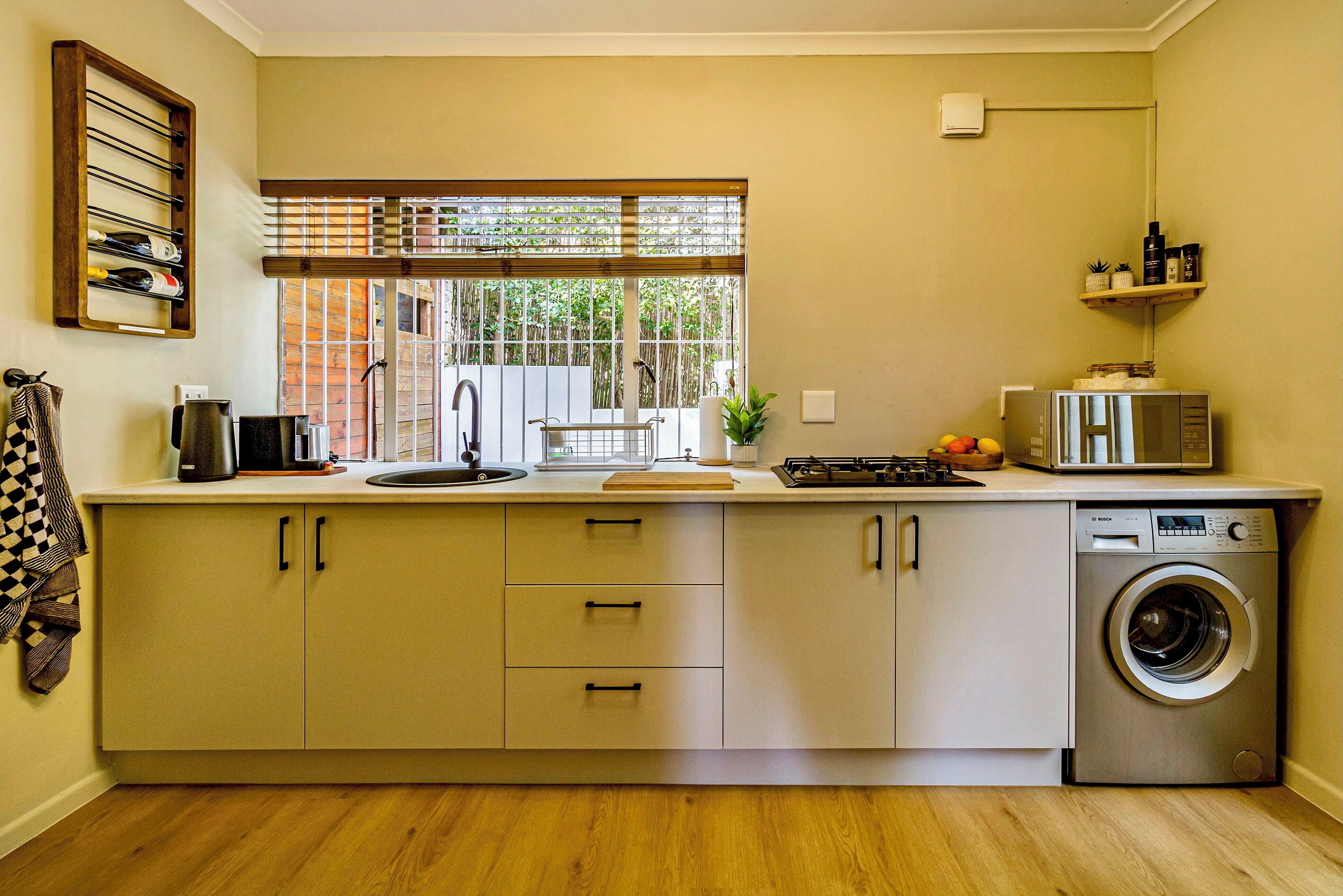 A compact kitchen with a built-in washing machine, a window with a view of greenery, and a microwave on the countertop.