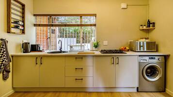 A compact kitchen with a built-in washing machine, a window with a view of greenery, and a microwave on the countertop.