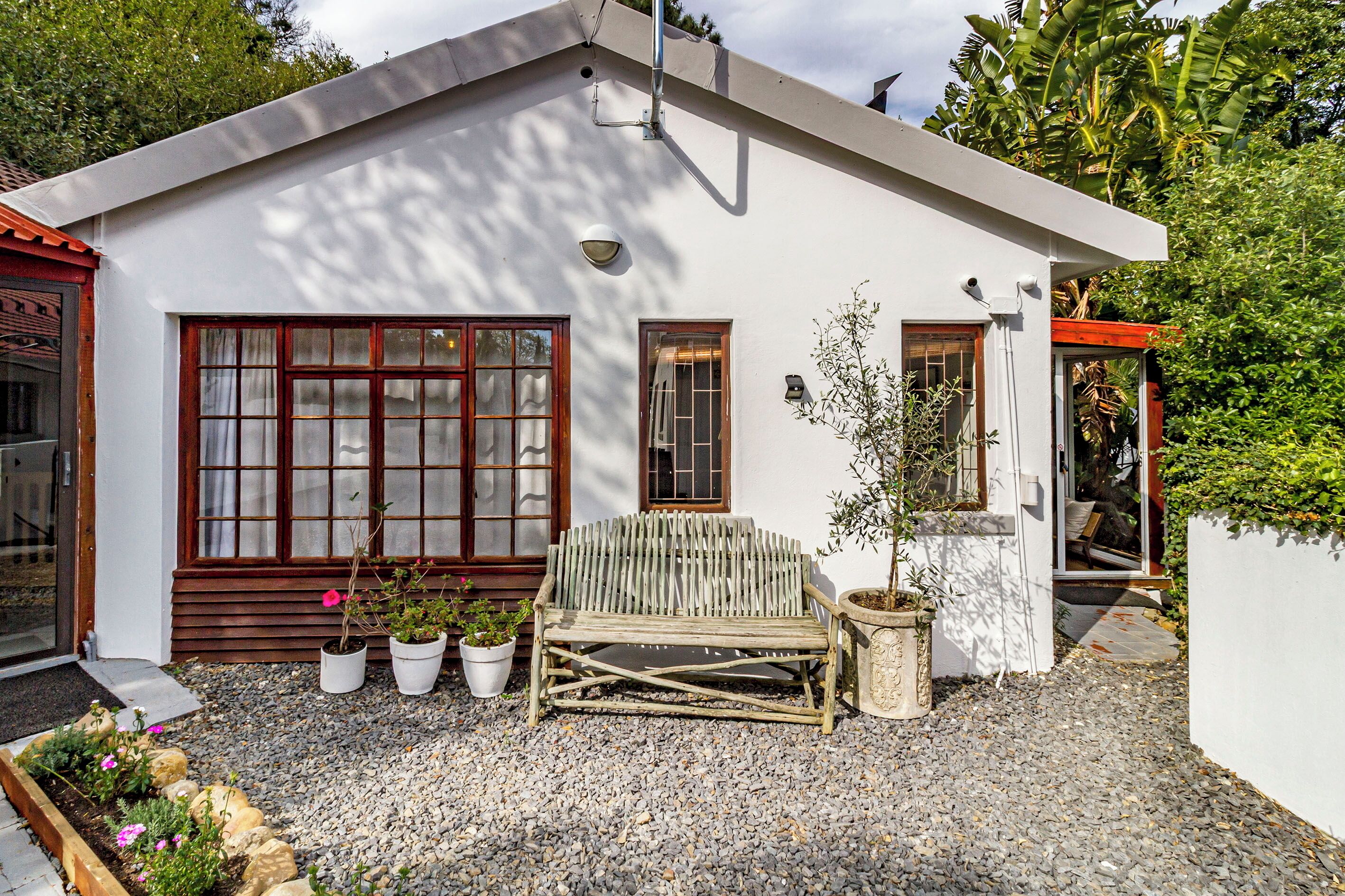 Una casa moderna con un banco de madera, plantas en macetas y un camino de entrada de grava.