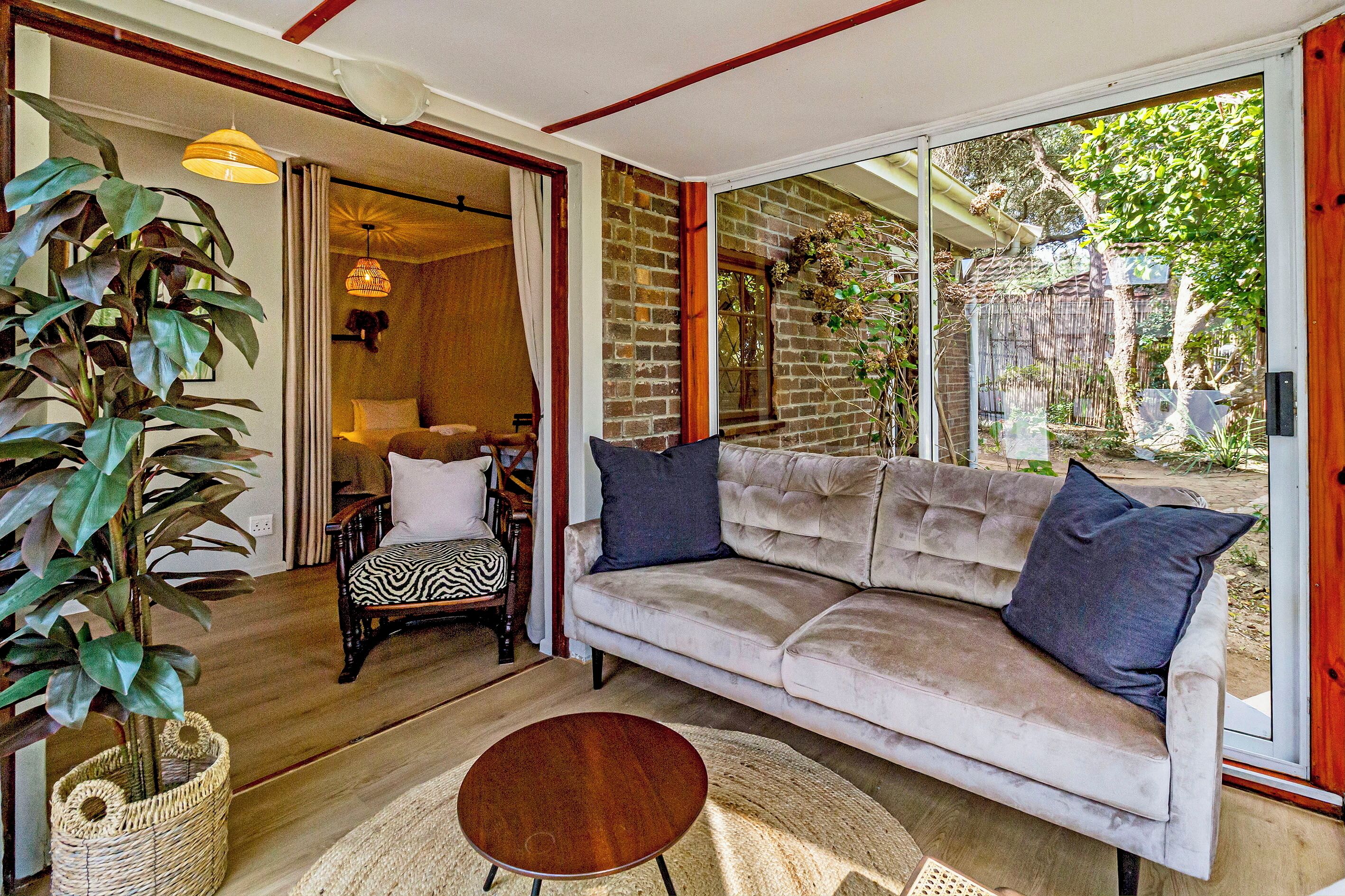 A living room with a sofa, a round coffee table, and a large plant. There is a sliding glass door leading to an outdoor area.