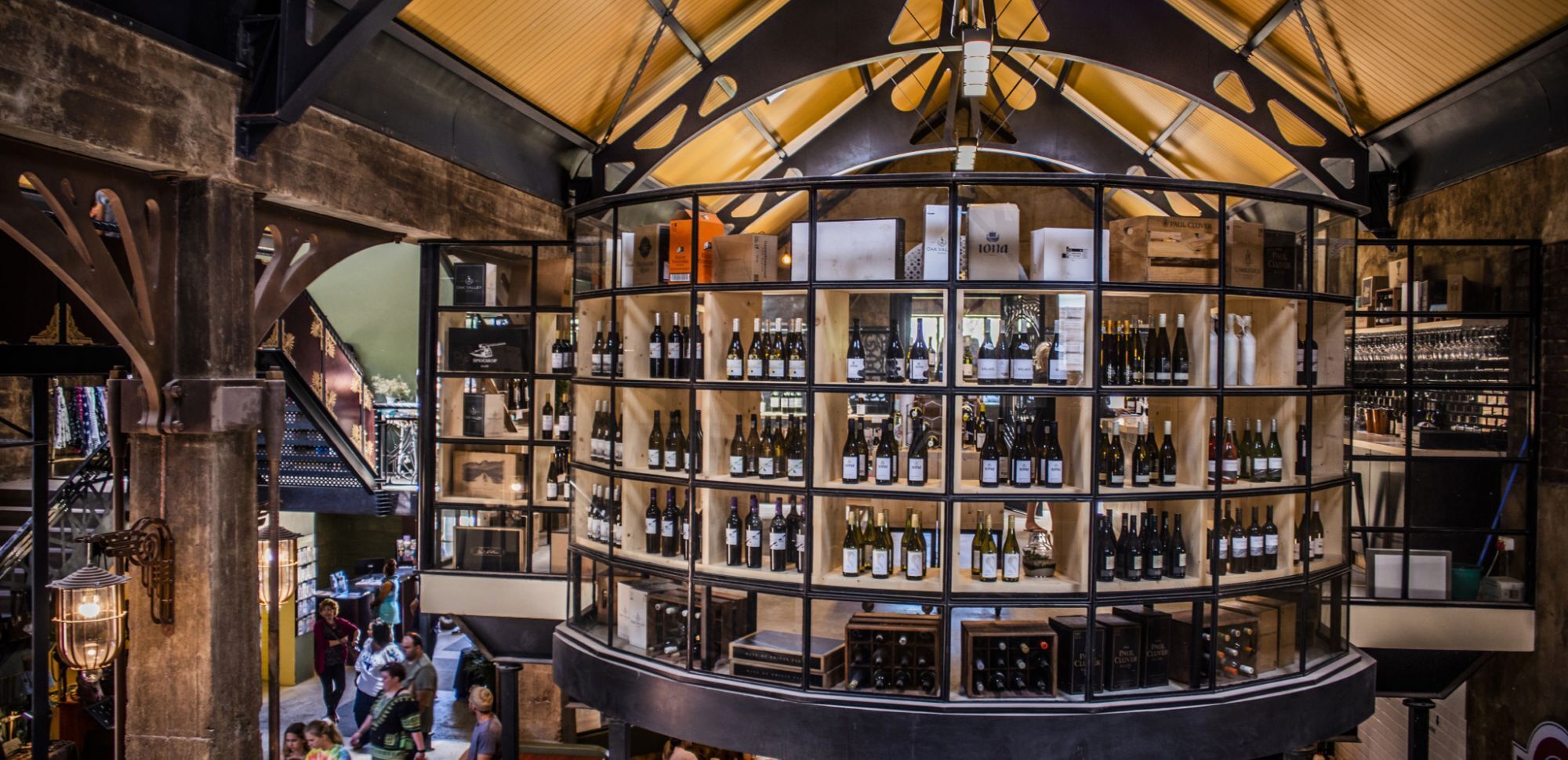 Una cantina vinicola circolare con numerose scaffalature piene di bottiglie, una scala a chiocciola e un arredamento rustico.