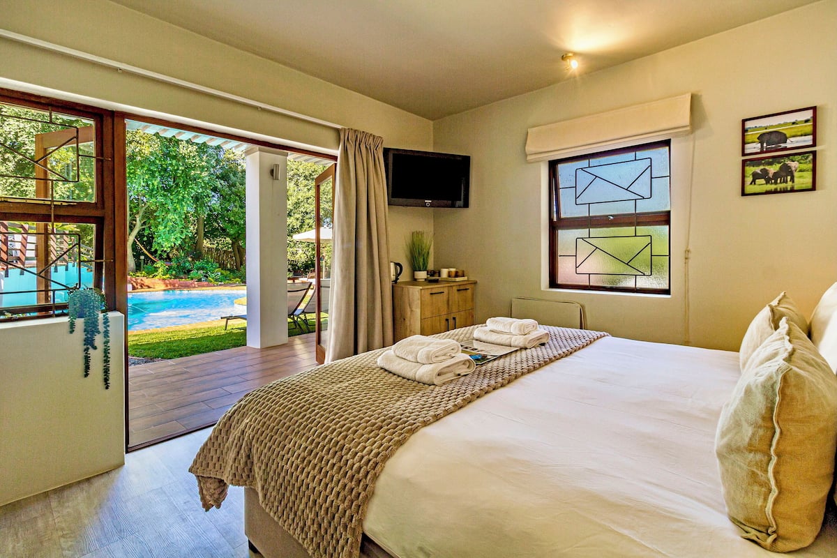 A bedroom with a large bed, a TV mounted on the wall, and a view of a pool outside.