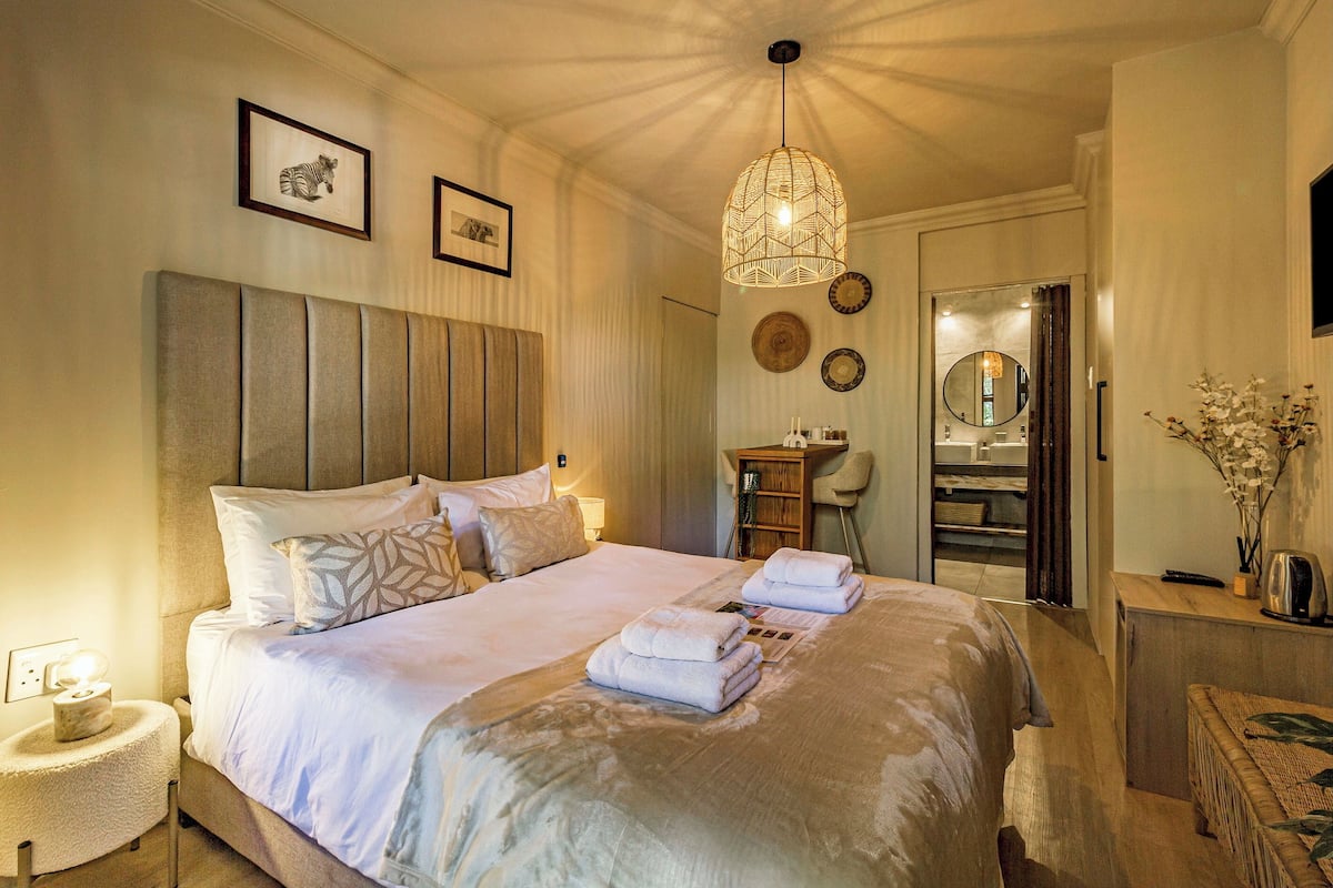 A well-lit bedroom with a large bed, bedside tables, a mirror, and a hanging light fixture.