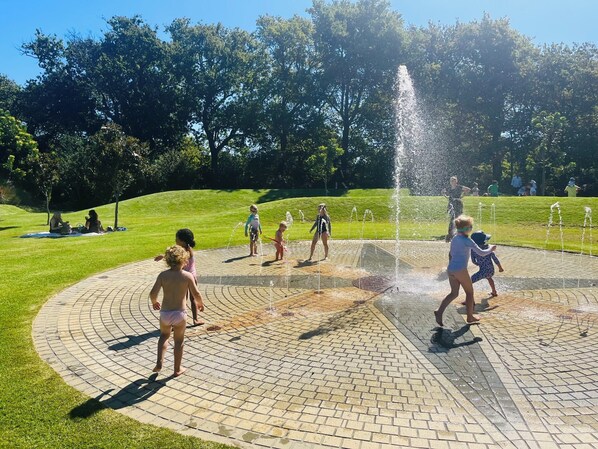 A public park with a water fountain area, paved walkways, and green grass. - Villa Helderberg (Cape Town)