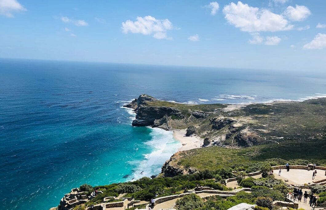 Un paysage côtier comprenant une falaise rocheuse, une plage et un espace d’observation agrémenté de sentiers et de constructions.