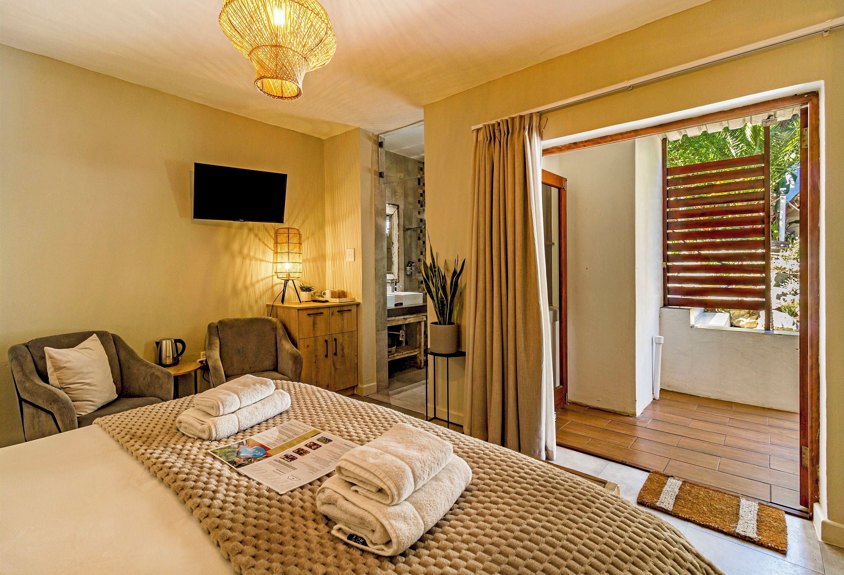 A hotel room with a bed, a TV, a desk with a lamp, a chair, and a view of the outside.
