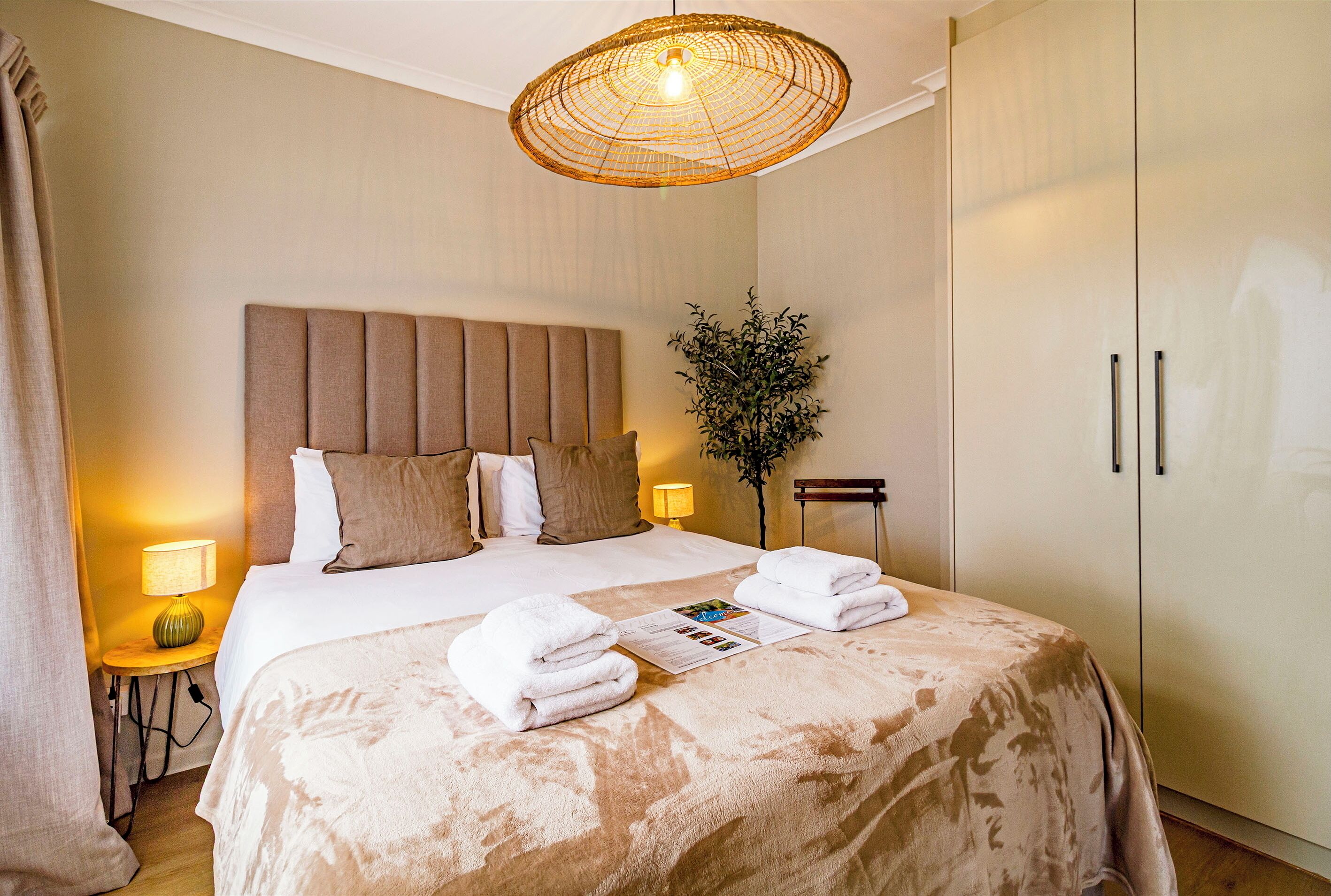 A neatly made bed with a large headboard, a bedside lamp, and a folded towel on the bed.