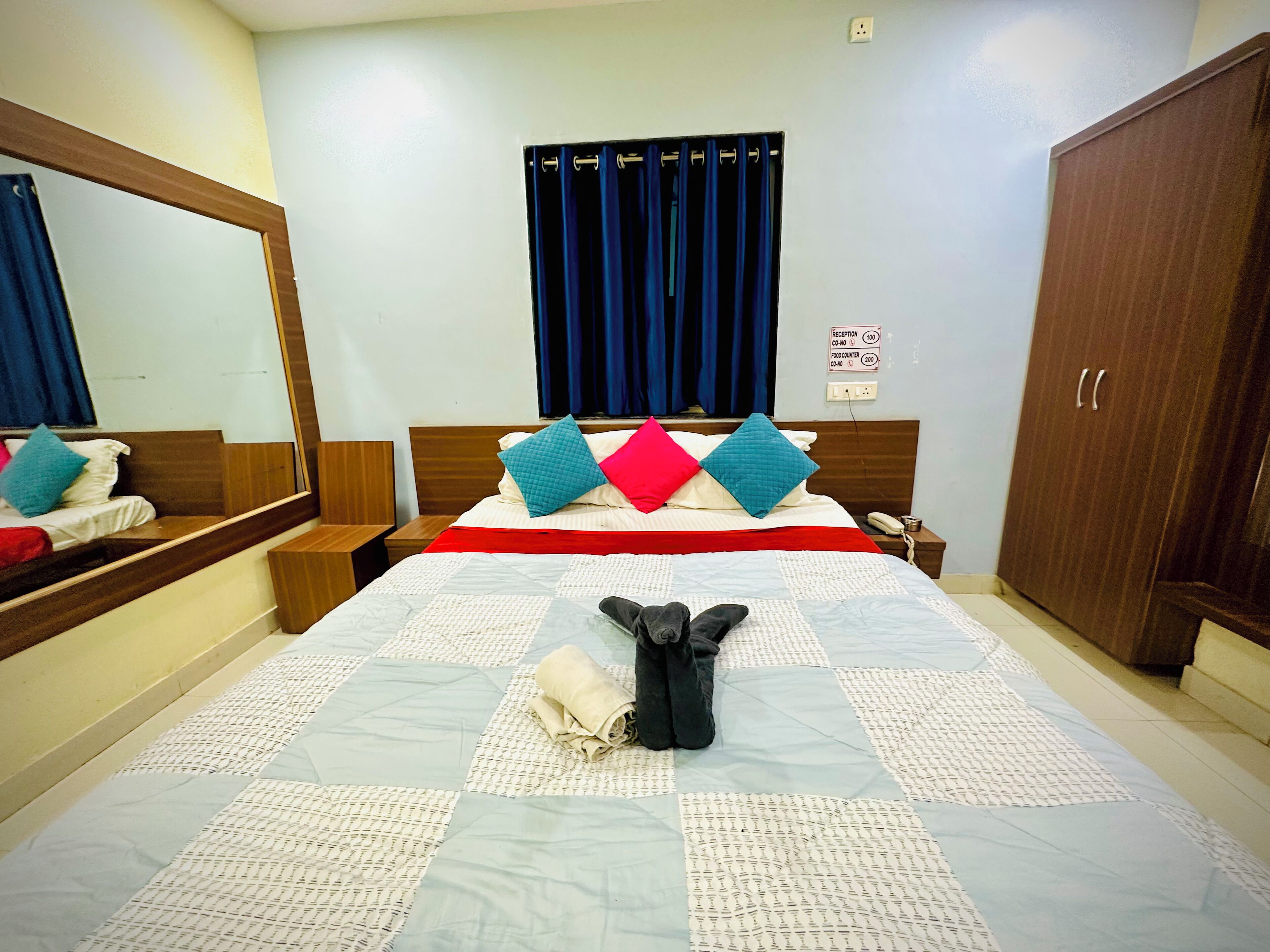 A hotel room with a bed, a mirror, a wardrobe, and a sign indicating the reception and food counter locations.