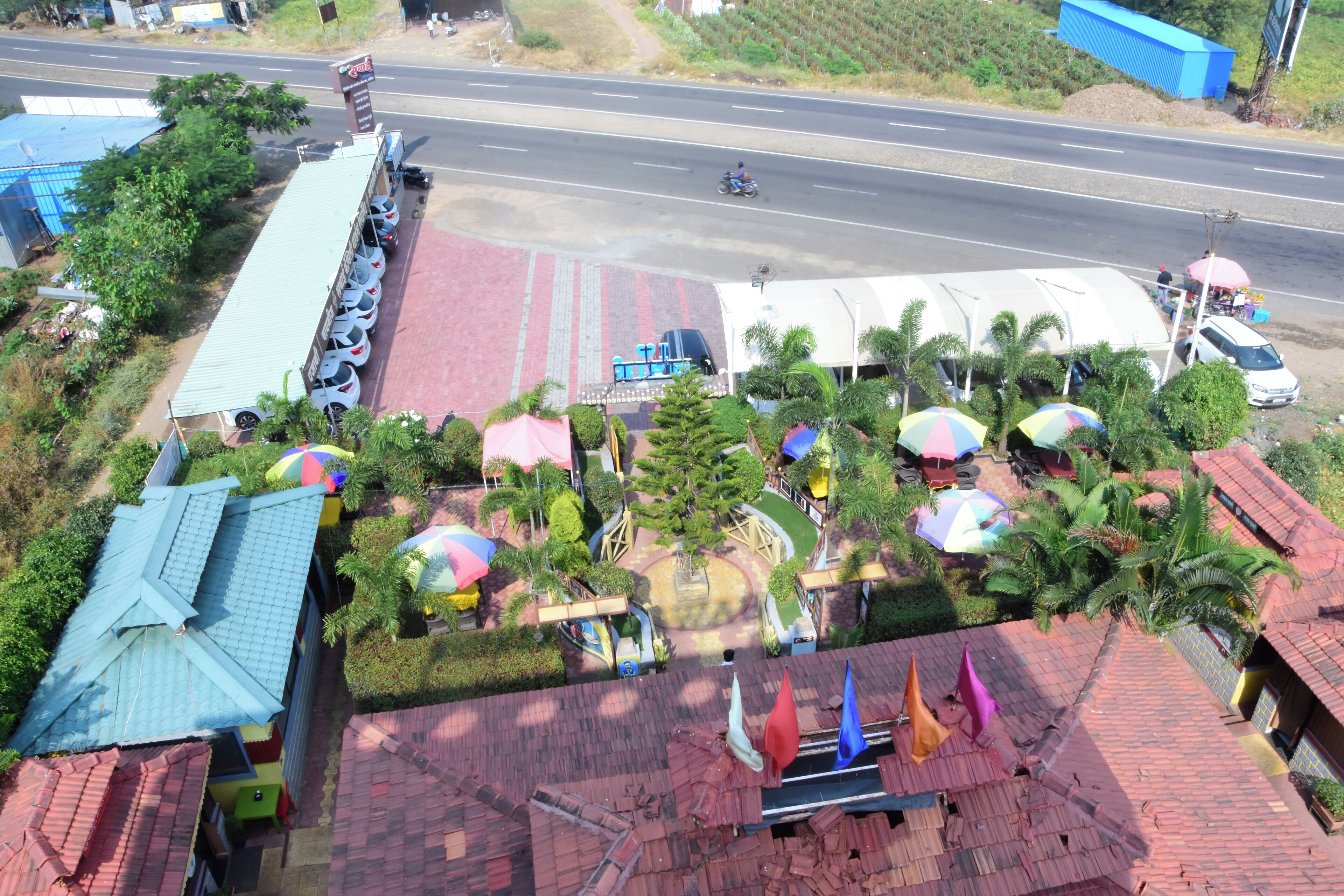 An aerial view of a commercial area with a parking lot, a road, and a row of shops.